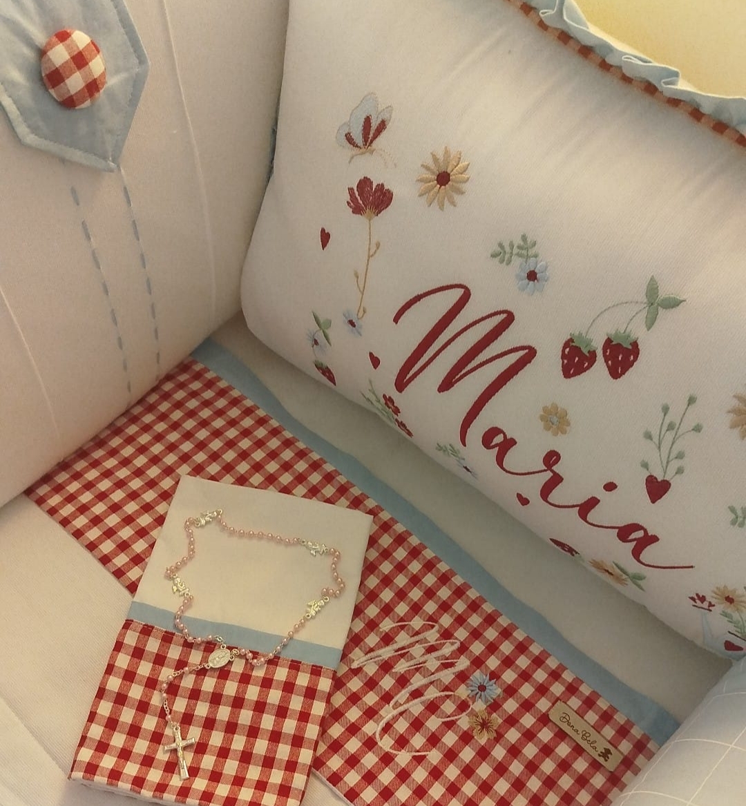 Uma foto do berço da bebê com uma almofada bordada com o nome Maria.